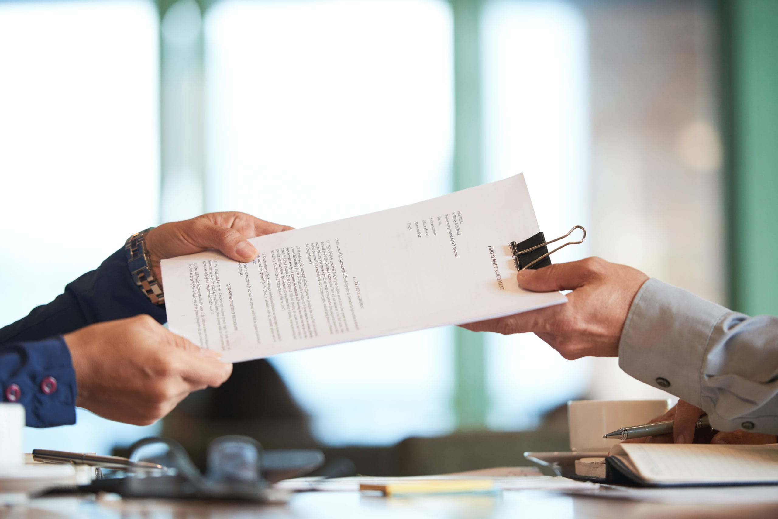 Hands exchanging a document with a paper clip, symbolizing property management agreements and compliance in real estate investment discussions.