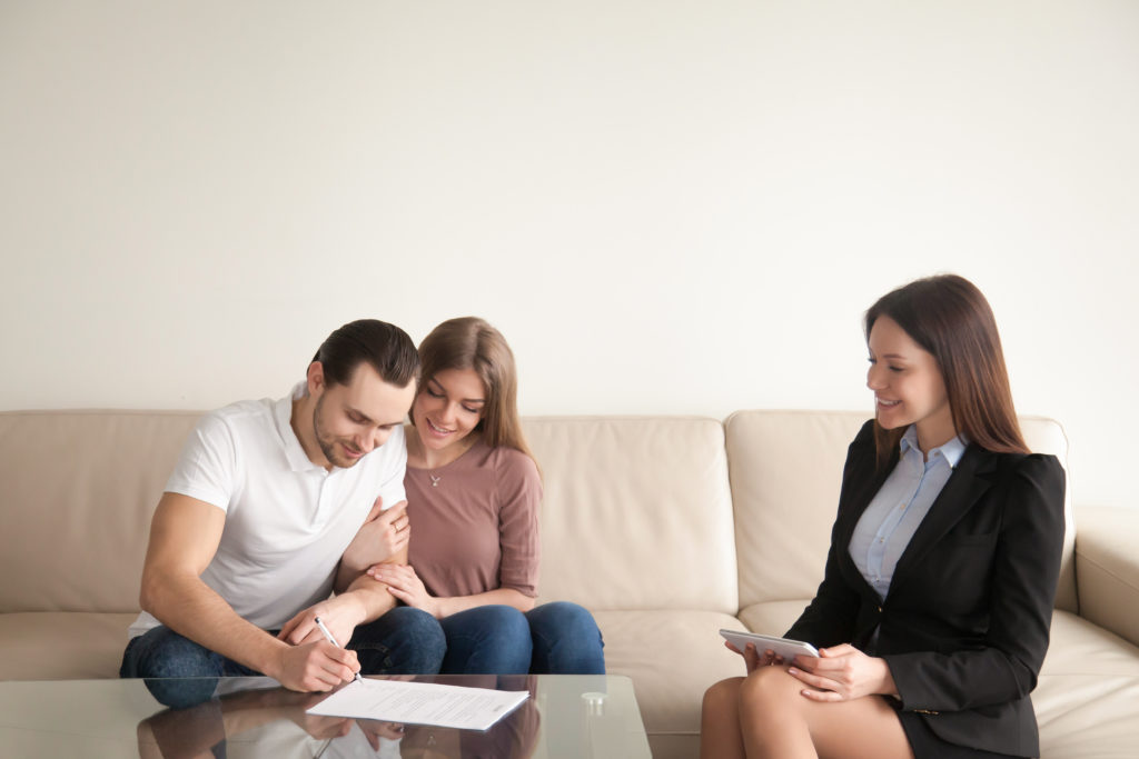 Happy young couple signing documents on meeting with real estate agent, young man putting signature on contract of purchase, buying property, first mortgage investment, prenuptial agreement