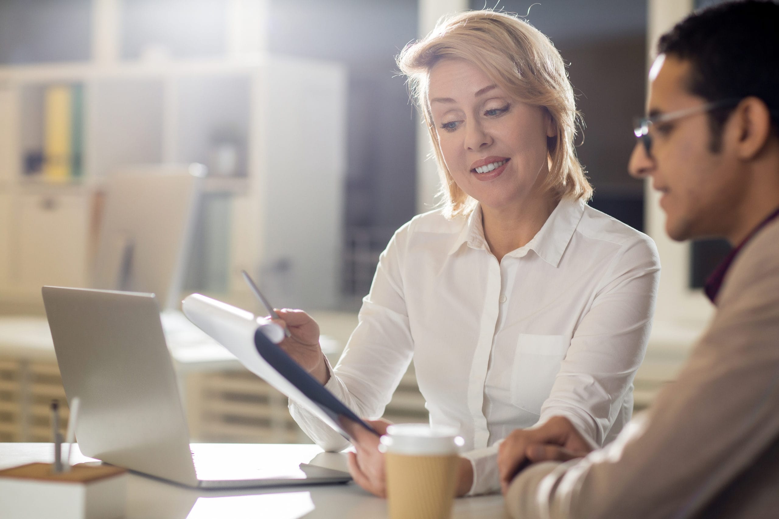 Professional woman discussing property management strategies with a man, laptop and coffee cup on the table, emphasizing collaboration for effective rental management.