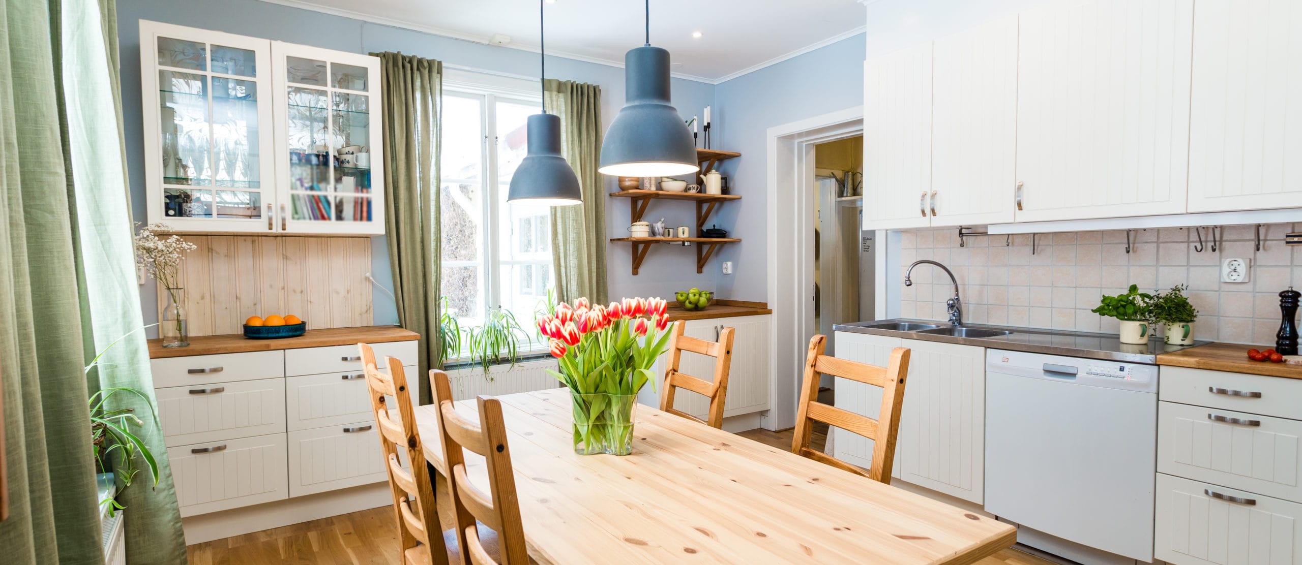 Bright and airy kitchen with wooden dining table, green curtains, and fresh tulips, emphasizing a welcoming atmosphere for property management discussions.