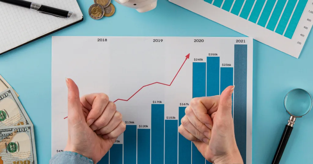 A person holding their thumbs up over a bar graph showing increasing profits over time