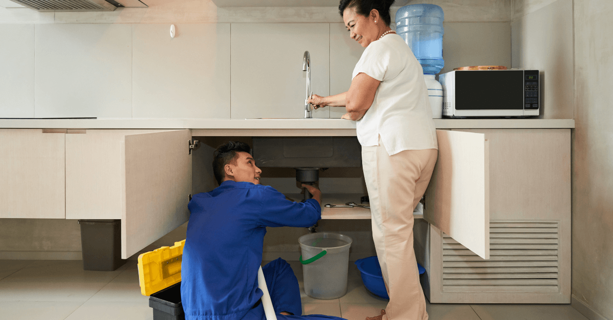 Plumber assisting a woman with kitchen sink maintenance, highlighting property management and maintenance issues for landlords.