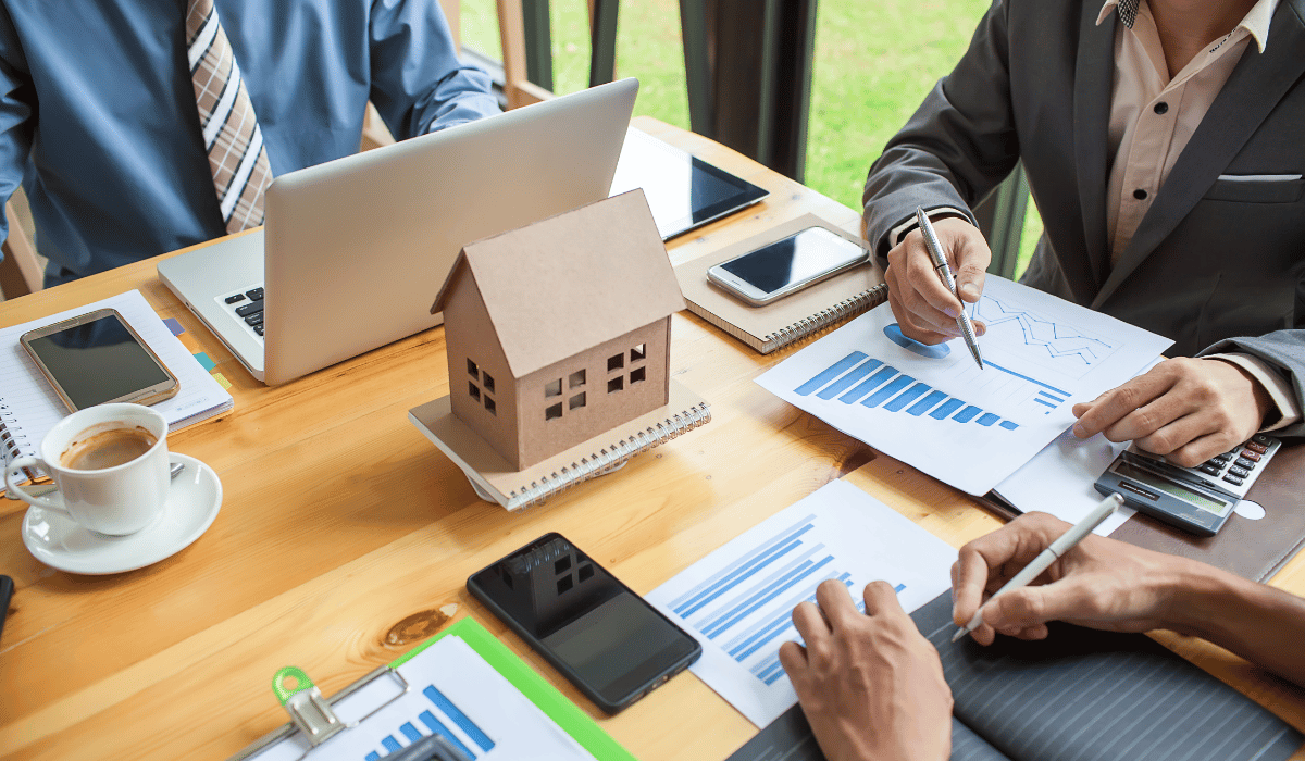 Business meeting analyzing property management budgets with charts, a model house, and financial documents.