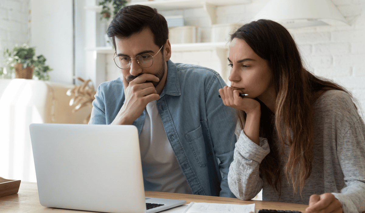 A couple are looking at a laptop. They appear concerned.