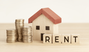 Stacks of coins next to a small wooden house and blocks that spell "RENT."