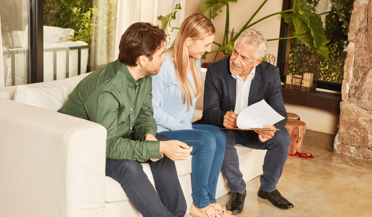 Three people are seated on a couch, likely discussing documents together.