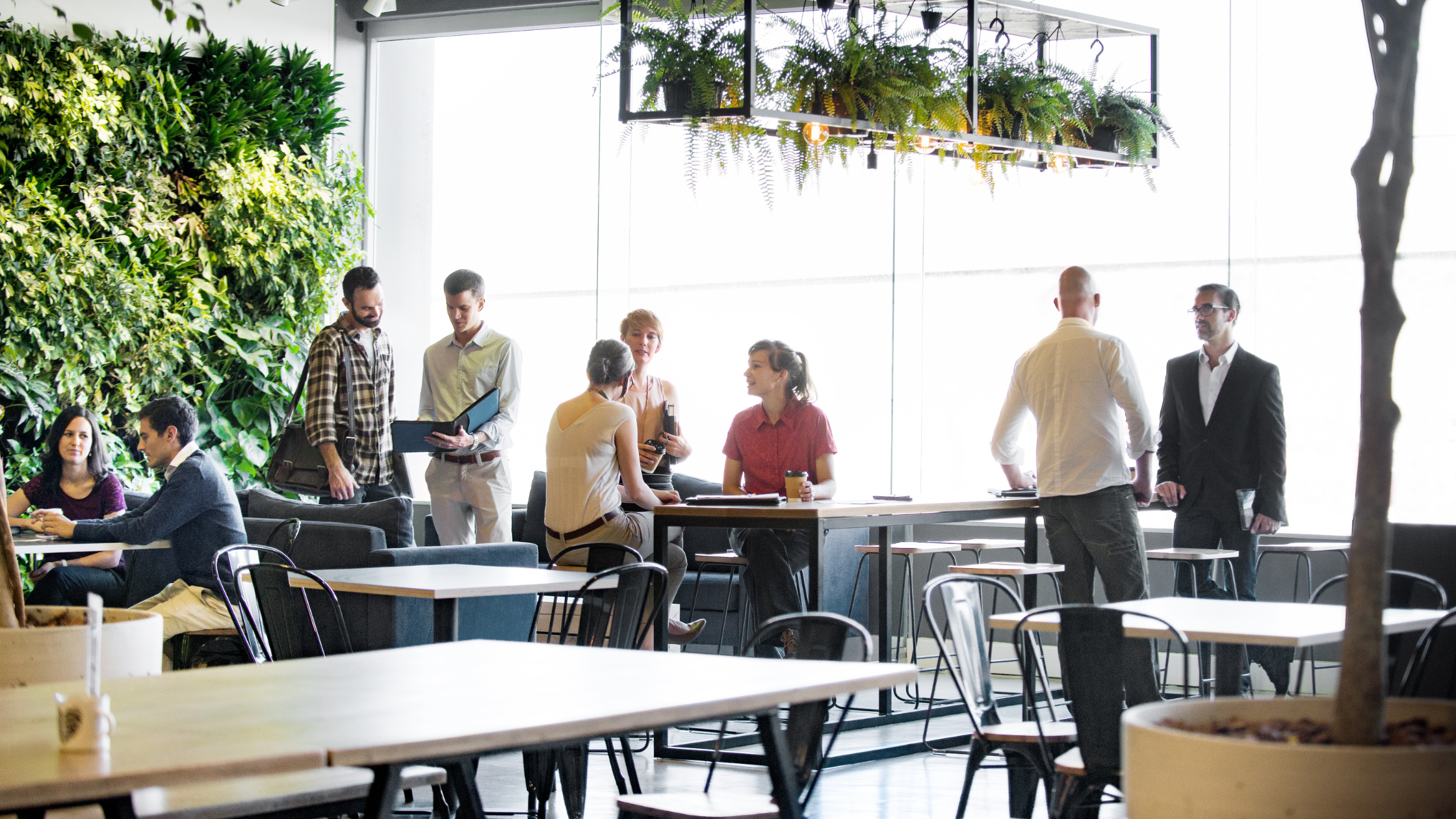 A diverse group of people casually meeting, some sitting at a table, others standing.
