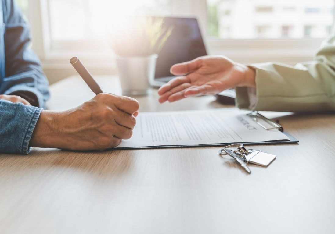 Boston landlord and tenant signing lease agreement at desk with documents and pen in bright professional office